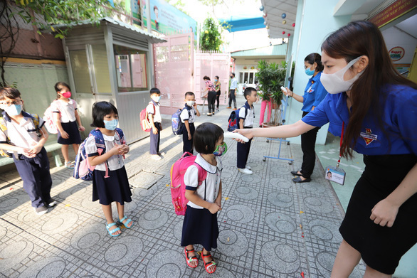 Học sinh lớp 1 Trường tiểu học Trần Bình Trọng (Q.5, TP.HCM) được các cô giáo đo thân nhiệt trước khi vào lớp sáng 11-5 - Ảnh: NHƯ HÙNG